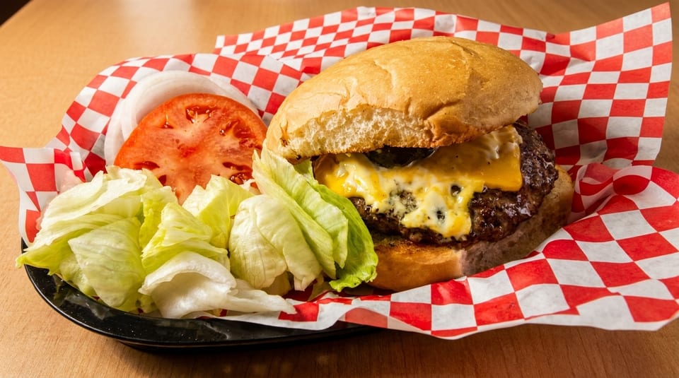 Cheeseburger with melted cheese, lettuce, tomato, and onion on a red and white checkered paper.